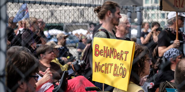 Menschen in einem Käfig, einer hält ein Schild mit der Aufschrift "Behindert nicht blöd"