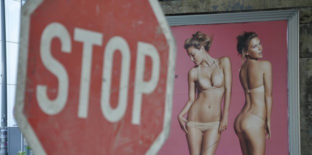 Im Hintergrund eine Frau im Bikini auf einem Werbeplakat. Davor ein Stop-Schild Im Hintergrund eine Frau im Bikini auf einem Werbeplakat. Davor ein Stop-Schild