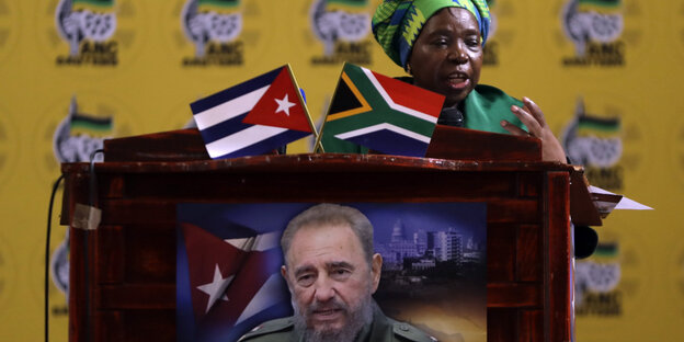 Eine Frau steht am Rednerpult, den eine südafrikanische und eine kubanische Flagge sowie ein Bild Fidel Castros schmücken Eine Frau steht am Rednerpult, den eine südafrikanische und eine kubanische Flagge sowie ein Bild Fidel Castros schmücken