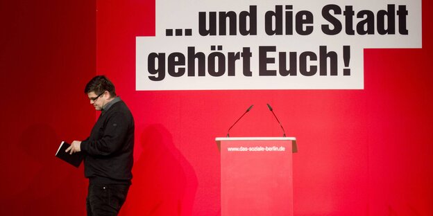 Andrej Holm steht neben einem Rednerpult und schaut in ein Buch Andrej Holm steht neben einem Rednerpult und schaut in ein Buch