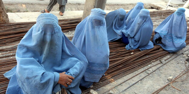 Sechs Frauen in hellblauen Burkas sitzen auf einem Stapel aus Metallstangen Sechs Frauen in hellblauen Burkas sitzen auf einem Stapel aus Metallstangen