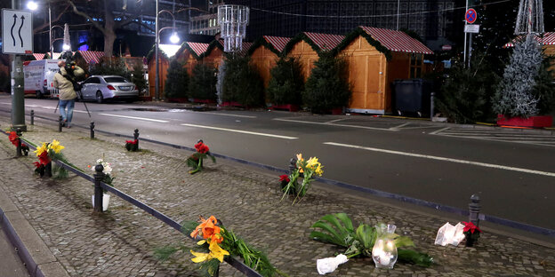 Es ist Nacht, vor geschlossenen Buden eines Weihnachtsmarkt liegen einzelne gebundene Blumensträuße Es ist Nacht, vor geschlossenen Buden eines Weihnachtsmarkt liegen einzelne gebundene Blumensträuße