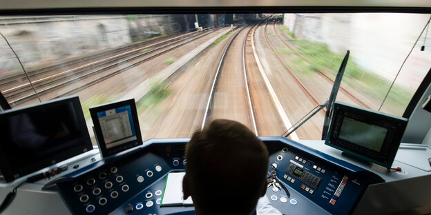 Blick auf den Hinterkopf eines Menschen im Fahrerhäuschen einer S-Bahn und die davorliegende Strecke Blick auf den Hinterkopf eines Menschen im Fahrerhäuschen einer S-Bahn und die davorliegende Strecke