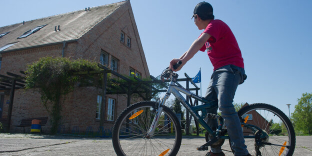 ein syrischer Junge auf einem Fahrrad vor einem verschlossen wirkenden Hof in Mecklenburg-Vorpommern ein syrischer Junge auf einem Fahrrad vor einem verschlossen wirkenden Hof in Mecklenburg-Vorpommern