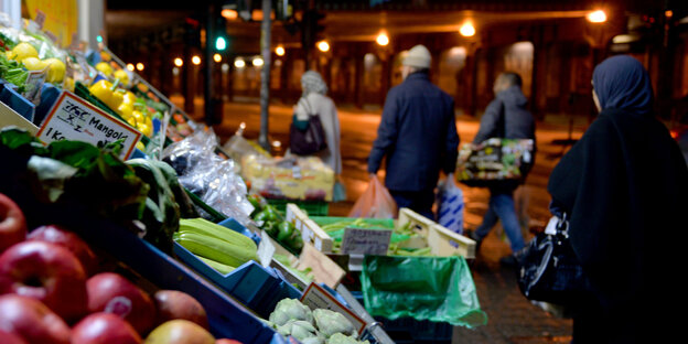 Obst und Gemüse liegt in einer Auslage, daneben laufen Menschen