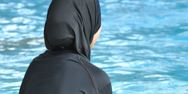 Ein Mädchen sitzt im Burkini in einem Schwimmbad Ein Mädchen sitzt im Burkini in einem Schwimmbad