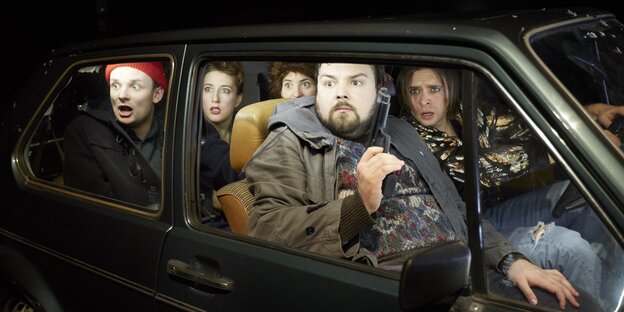 Vier Schauspieler sitzen in einem Auto, einer hat eine Pistole in der Hand Vier Schauspieler sitzen in einem Auto, einer hat eine Pistole in der Hand