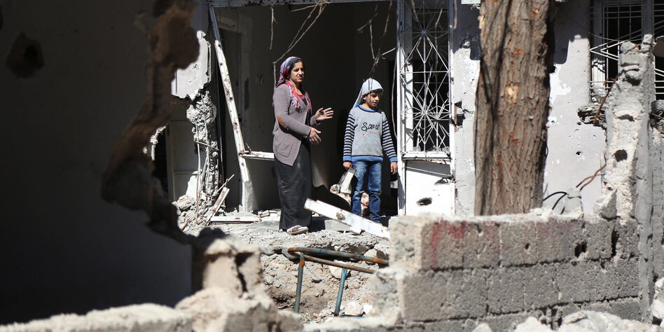 Sokağa çıkma yasaklarının ardından Cizre'de yıkılmış bir evden dışarıya bakan anne ve çocuk