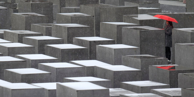 Die Stelen des Holocaust-Mahnmals sind mit Schnee bedeckt, zwischen ihnen steht eine Frau mit einem roten Regenschirm