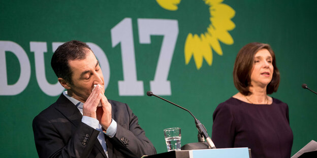 Cem Özdemir und Katrin Göhring-Eckhardt stehen vor dem Grünen-Logo. Cem Özdemir putzt sich die Nase Cem Özdemir und Katrin Göhring-Eckhardt stehen vor dem Grünen-Logo. Cem Özdemir putzt sich die Nase