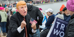 Ein Mensch trägt bei einer Demonstration eine Trump-Maske mit verlängerter Nase