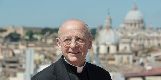 Ein Mann im Priestergewand. Im Hintergrund der Petersdom in Rom