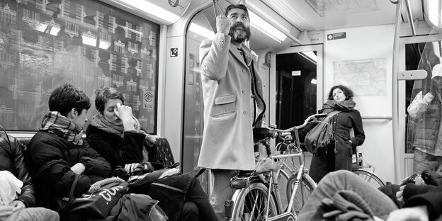 In einer U-Bahn: Zwei Frauen sitzen, ein Mann hält sich am Griff fest und steht In einer U-Bahn: Zwei Frauen sitzen, ein Mann hält sich am Griff fest und steht