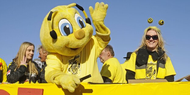 Emma, das Maskottchen des BVB neben zwei Fans