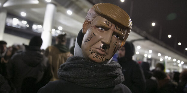 Jemand trägt auf dem Hinterkopf eine Trump-Maske mit einem Hitlerbärtchen Jemand trägt auf dem Hinterkopf eine Trump-Maske mit einem Hitlerbärtchen