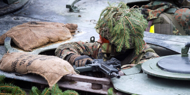 Ein Soldat mit Schminke im Gesicht und Tannenzweigen auf dem Kopf schaut aus einer Panzerluke Ein Soldat mit Schminke im Gesicht und Tannenzweigen auf dem Kopf schaut aus einer Panzerluke