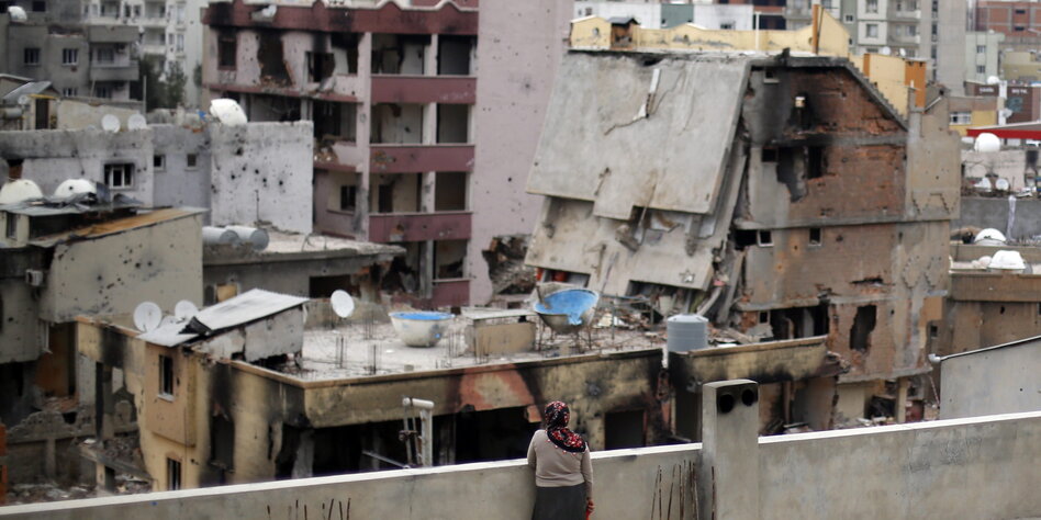 Eine Frau steht auf dem Dach und schaut sich die Trümmer ihrer Stadt