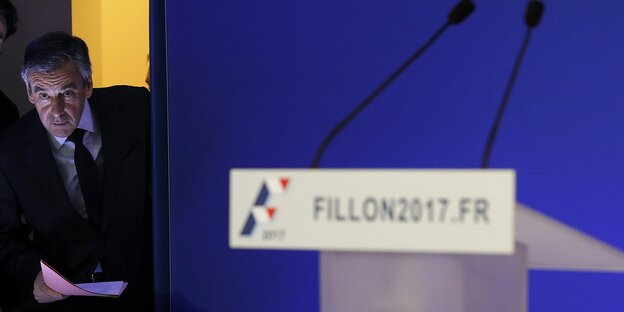 Ein leeres Rednerpult. Im Hintergrund schaut François Fillon durch die Kulissen hindurch Ein leeres Rednerpult. Im Hintergrund schaut François Fillon durch die Kulissen hindurch