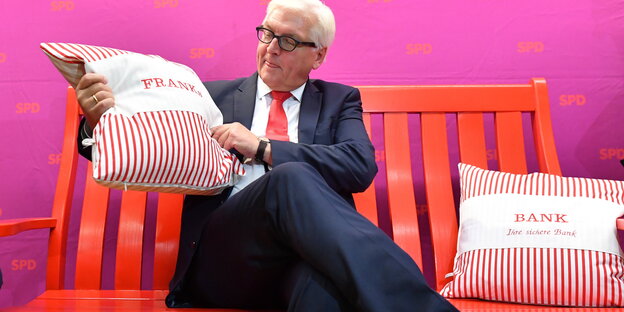 Frank-Walter Steinmeier sitzt mit zwei Kissen, auf denen "Franks Bank" steht, auf einer roten Bank Frank-Walter Steinmeier sitzt mit zwei Kissen, auf denen "Franks Bank" steht, auf einer roten Bank
