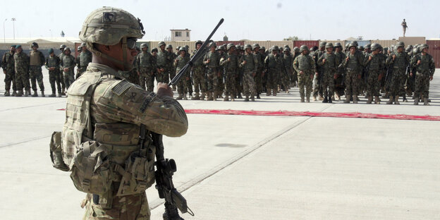 Ein US-Soldat in Kampfausrüstung und mit Maschinengewehr vor einer Truppe anderer Soldaten Ein US-Soldat in Kampfausrüstung und mit Maschinengewehr vor einer Truppe anderer Soldaten