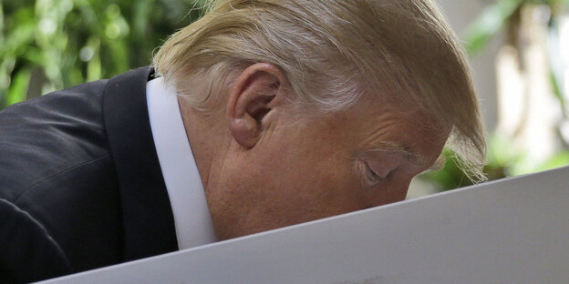 Donald Trump beugt sich über ein Rednerpult das sein Profil halb verdeckt Donald Trump beugt sich über ein Rednerpult das sein Profil halb verdeckt