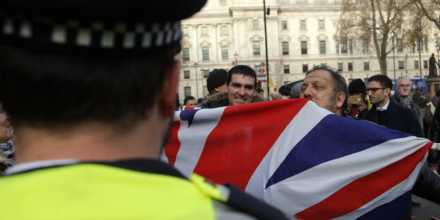 Ein Polizist steht vor Demonstranten mit einer britischen Fahne Ein Polizist steht vor Demonstranten mit einer britischen Fahne