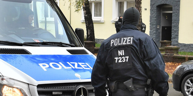 Ein maskierter Polizist steht neben einem Polizeiauto Ein maskierter Polizist steht neben einem Polizeiauto