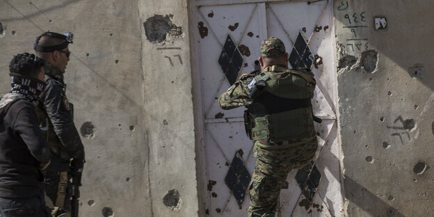 schwer bewaffnet stehen drei Soldaten vor einer von Schüssen durchlöcherten Hauswand schwer bewaffnet stehen drei Soldaten vor einer von Schüssen durchlöcherten Hauswand