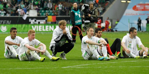 Mehrere Fußballleute sitzen auf dem Rasen und gucken nach vorne Mehrere Fußballleute sitzen auf dem Rasen und gucken nach vorne