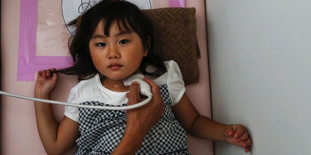 Ein kleines japanisches Mädchen liegt auf einer Liege und wird am Kehlkopf untersucht Ein kleines japanisches Mädchen liegt auf einer Liege und wird am Kehlkopf untersucht
