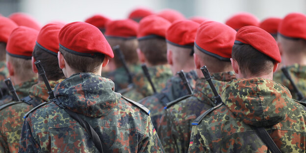 Menschen in Tarnuniform und mit roten Barretten von hinten