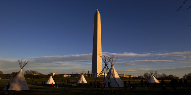 vorne Tipis, im Hindergrund eine Stadt und ein riesiger Obelisk vorne Tipis, im Hindergrund eine Stadt und ein riesiger Obelisk