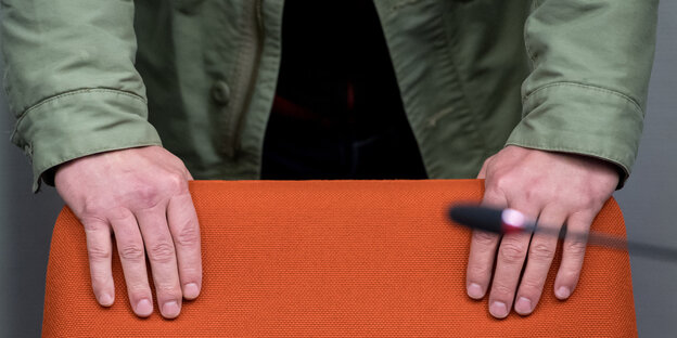 Zwei Hände halten die Rückenlehne eines orangefarbenen Stuhls Zwei Hände halten die Rückenlehne eines orangefarbenen Stuhls