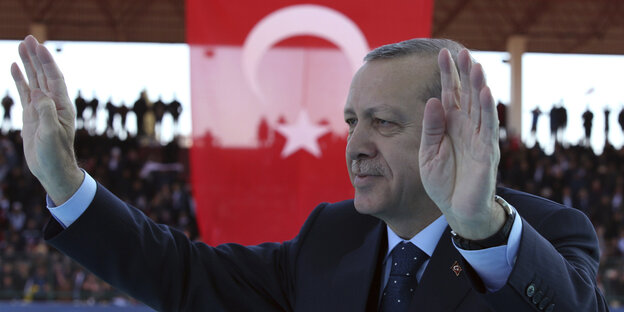 Erdogan steht vor einer türkischen Flagge und hebt messianisch beide Hände Erdogan steht vor einer türkischen Flagge und hebt messianisch beide Hände