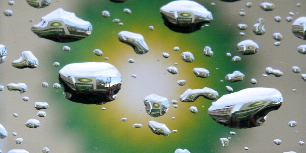 Im Hintergrund ein gelb-grüner Kreis, im Vordergrund große Regentropfen auf einer Glasscheibe