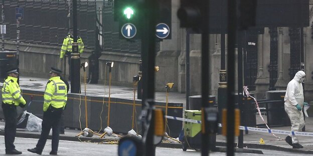 Eine Straße mit vielen Ampeln, die nicht von Autos befahren wird. Stattdessen sind Männer in gelben Warnwesten und Menschen in weißen Ganzkörperanzügen zu sehen Eine Straße mit vielen Ampeln, die nicht von Autos befahren wird. Stattdessen sind Männer in gelben Warnwesten und Menschen in weißen Ganzkörperanzügen zu sehen
