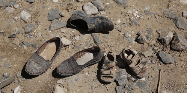 Ein paar große Schuhe und ein Paar Kinderschuhe liegen auf staubigem Boden Ein paar große Schuhe und ein Paar Kinderschuhe liegen auf staubigem Boden