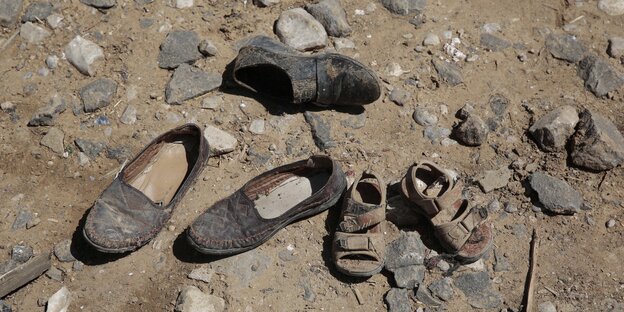 Ein paar große Schuhe und ein Paar Kinderschuhe liegen auf staubigem Boden