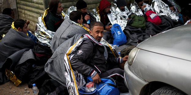 Mehrere Flüchtlinge sitzen auf dem Boden und tragen Wärmedecken Mehrere Flüchtlinge sitzen auf dem Boden und tragen Wärmedecken