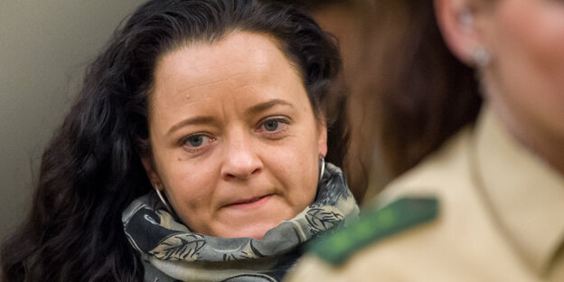 Beate Zschäpe mit dickem grauen Schal hinter einer Polizeibeamtin Beate Zschäpe mit dickem grauen Schal hinter einer Polizeibeamtin