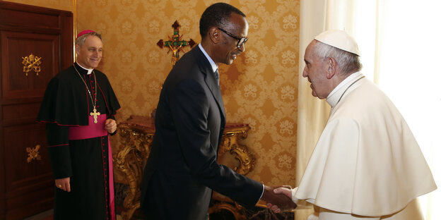 Rechts im Bild ein alter Mann in Papst-Kleidung, in der Mitte ein Mann in Anzug, der ihm die Hand gibt, ganz links im Bild ein Mann in Kardinals-Kleidung, der lacht Rechts im Bild ein alter Mann in Papst-Kleidung, in der Mitte ein Mann in Anzug, der ihm die Hand gibt, ganz links im Bild ein Mann in Kardinals-Kleidung, der lacht