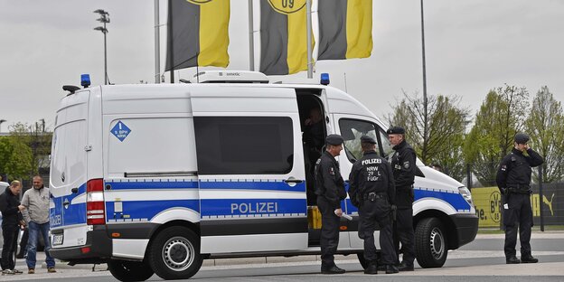 Polizisten stehen uniformiert vor einem Einsatzwagen, dahinter BVB-Logos Polizisten stehen uniformiert vor einem Einsatzwagen, dahinter BVB-Logos