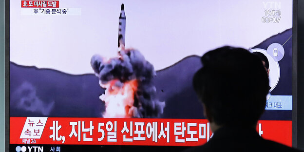 Rückansicht eines Kopfes vor einem Bildschirm, der Aufnahmen eines Raketenstarts zeigt Rückansicht eines Kopfes vor einem Bildschirm, der Aufnahmen eines Raketenstarts zeigt