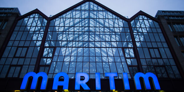 Ein gläsernes Haus von unten fotografiert, im unteren Teil des Bildes blaue Buchstaben, die das Wort Maritim formen Ein gläsernes Haus von unten fotografiert, im unteren Teil des Bildes blaue Buchstaben, die das Wort Maritim formen