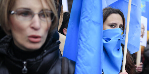 Zwei Frauen in warmen Winterjacken mit blauen, zusammengerollten Fahnen, eine hat auch eine blaue Fahne vor den Mund gebunden Zwei Frauen in warmen Winterjacken mit blauen, zusammengerollten Fahnen, eine hat auch eine blaue Fahne vor den Mund gebunden