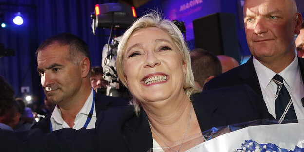 Marine Le Pen lächelt, umrahmt von zwei Sicherheitsleuten Marine Le Pen lächelt, umrahmt von zwei Sicherheitsleuten