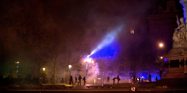 Im schwachen Licht von Straßenlaternen sind Rauchschwaden und Demonstranten zu erkennen