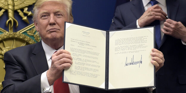 Trump hält Dokument mit seiner Unterschrift hoch und guckt siegessicher Trump hält Dokument mit seiner Unterschrift hoch und guckt siegessicher