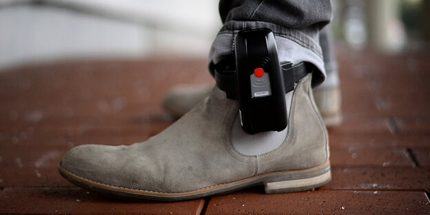 Männerschuhe - knapp drüber eine elektronische Fußfessel am Bein Männerschuhe - knapp drüber eine elektronische Fußfessel am Bein