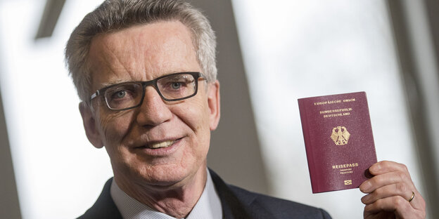 Ein Mann mit Brille hält lächelnd seinen deutschen Pass in die Höhe Ein Mann mit Brille hält lächelnd seinen deutschen Pass in die Höhe
